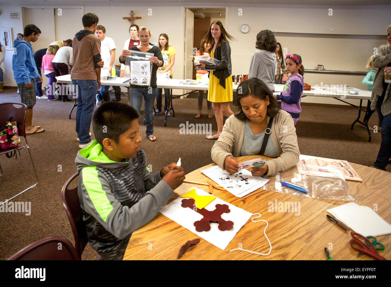 Hispanische Gemeindemitglieder im Gemeindesaal ein Laguna Niguel, CA, katholische Kirche, erste Heilige Eucharistie Banner als Pew Marker für Erstkommunion Zeremonien verwendet werden. Stockfoto