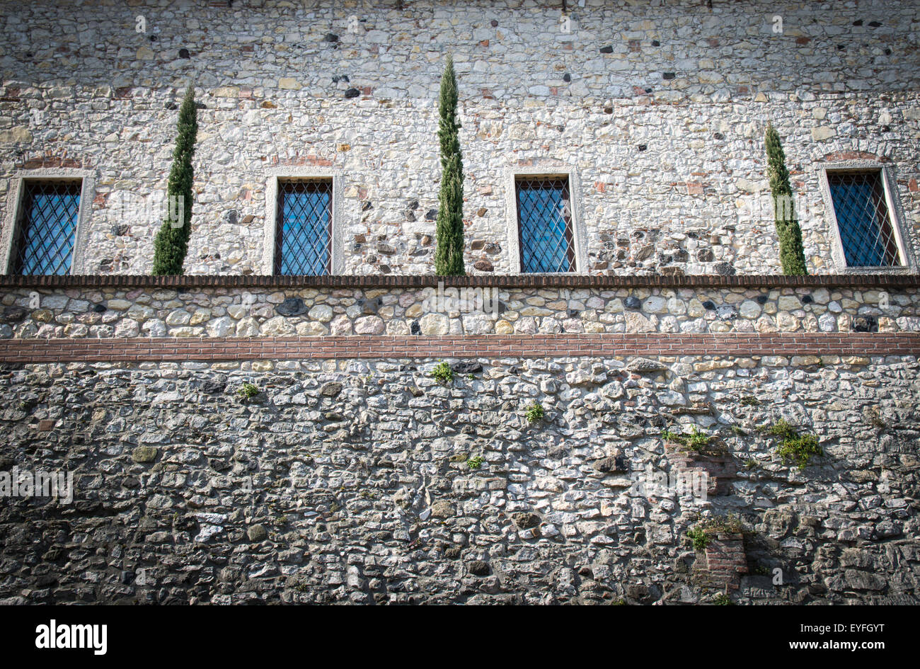 Steinmauer einer mittelalterlichen Festung mit vier Fenstern und einem kleinen hängenden Garten. Stockfoto