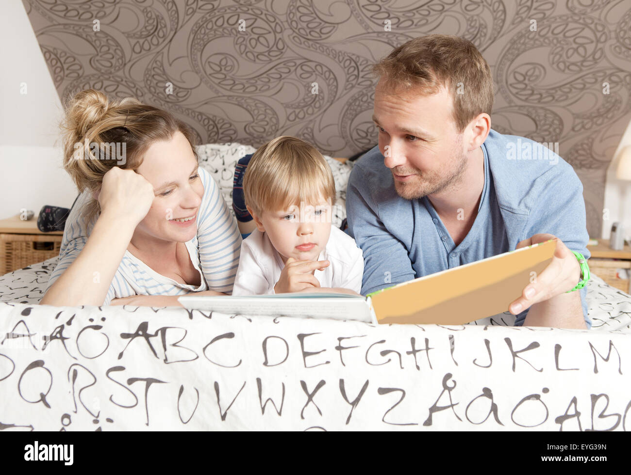 eine Familie auf dem Bett liegen und ein Buch zu lesen Stockfoto