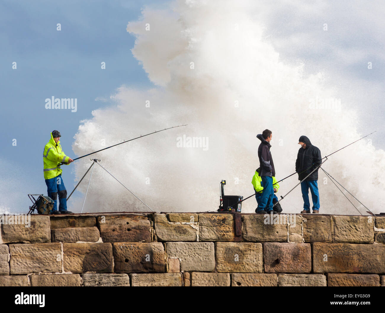 Menschen der Fischerei von Seaham Pier an einem stürmischen Tag mit riesigen Welle am Pier Wand hinter brechen. Seaham, County Durham, England, UK Stockfoto