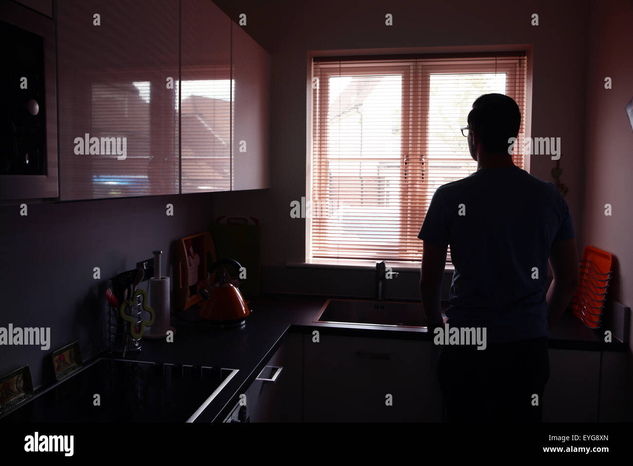 Junger Mann in einer Küche mit Blick durch ein Fenster Blind. Landschaft-Form. Stockfoto