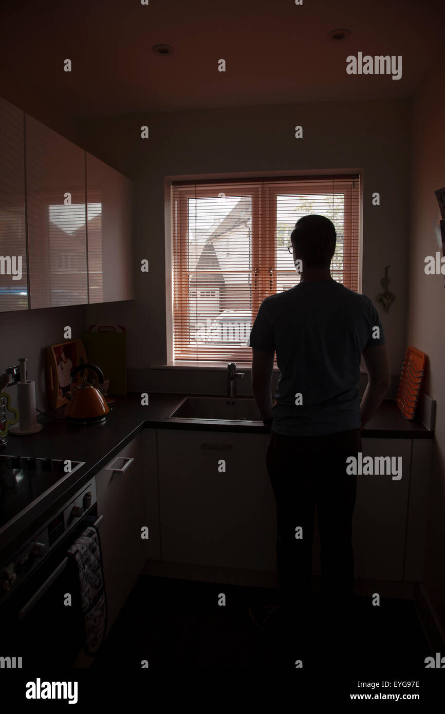 Junger Mann in einer Küche mit Blick durch ein Fenster Blind. Porträt-Form. Stockfoto