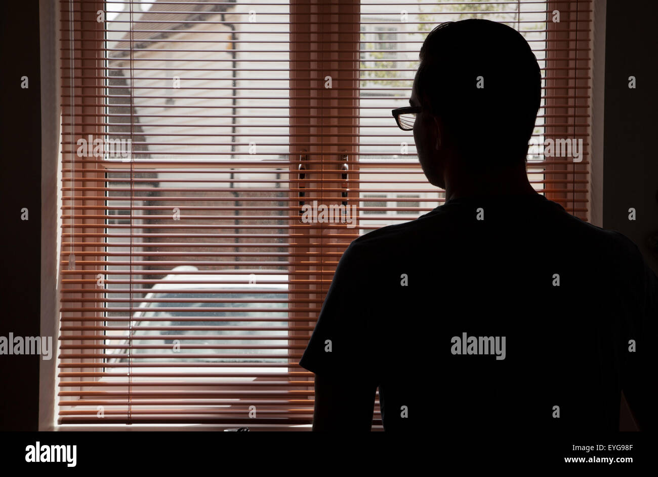 Junger Mann in einer Küche mit Blick durch ein Fenster Blind. Stockfoto