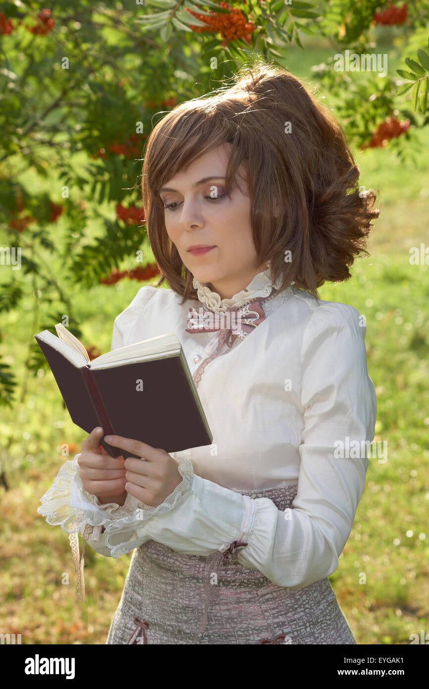 Gekleidet in Retro-Kleidung schönes Mädchen liest Buch mit leichten Lächeln auf ihrem Gesicht Stockfoto