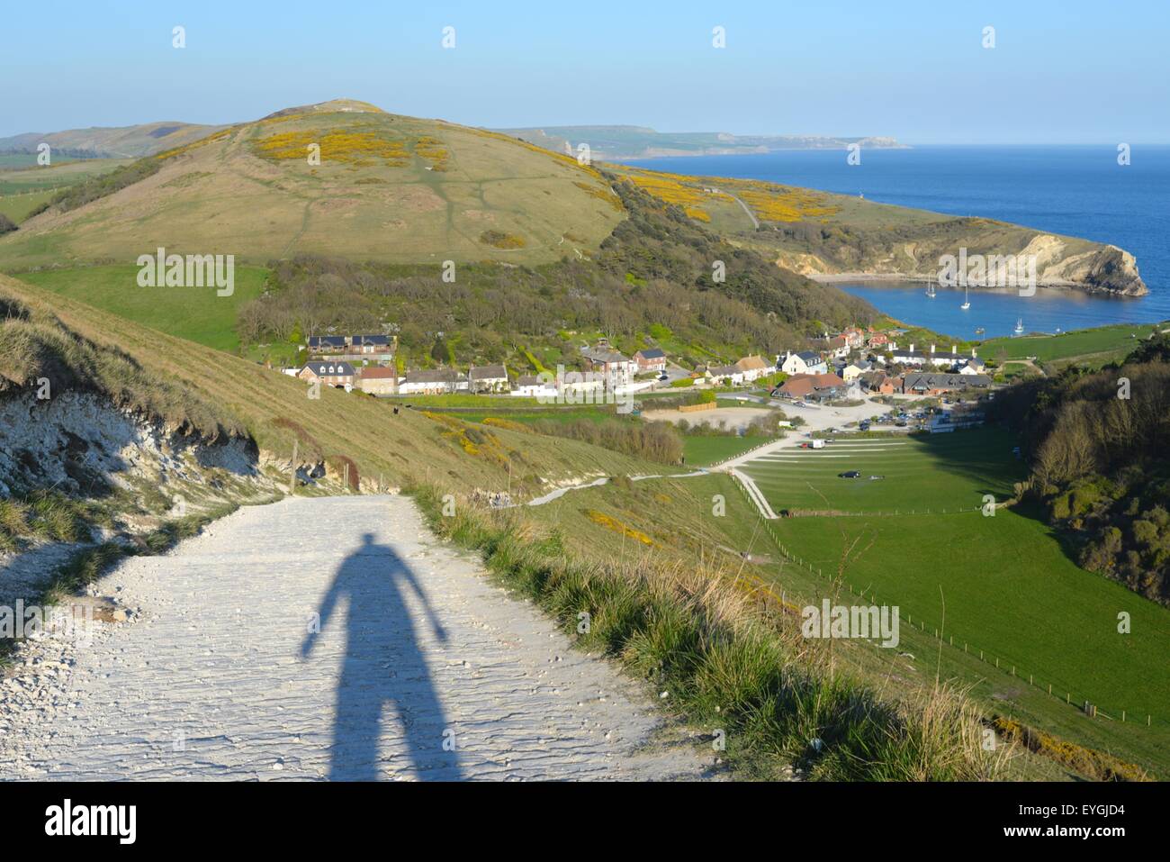 Am späten Nachmittag oder Abend wirft die Sonne einen menschlichen Schatten auf dem Pfad den Hügel hinunter nach Lulworth Cove, Dorset, Großbritannien. Stockfoto