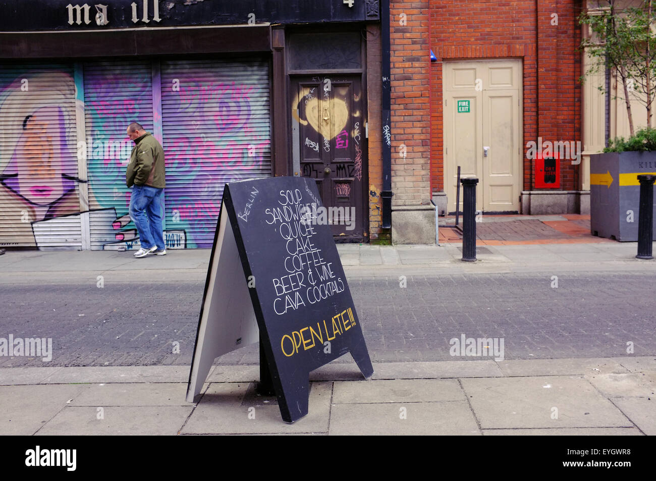 Ein Café-Sandwich-Board und ein Mann zu Fuß vorbei an Graffitied Metall Verschluss auf einer Straße in Dublin. Stockfoto