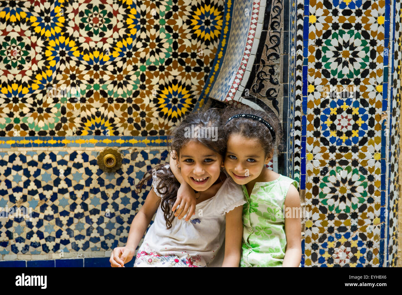 Zwei lächelnde Mädchen vor einer Wand mit bunten Fliesen, Souk, Fes, Marokko Stockfoto