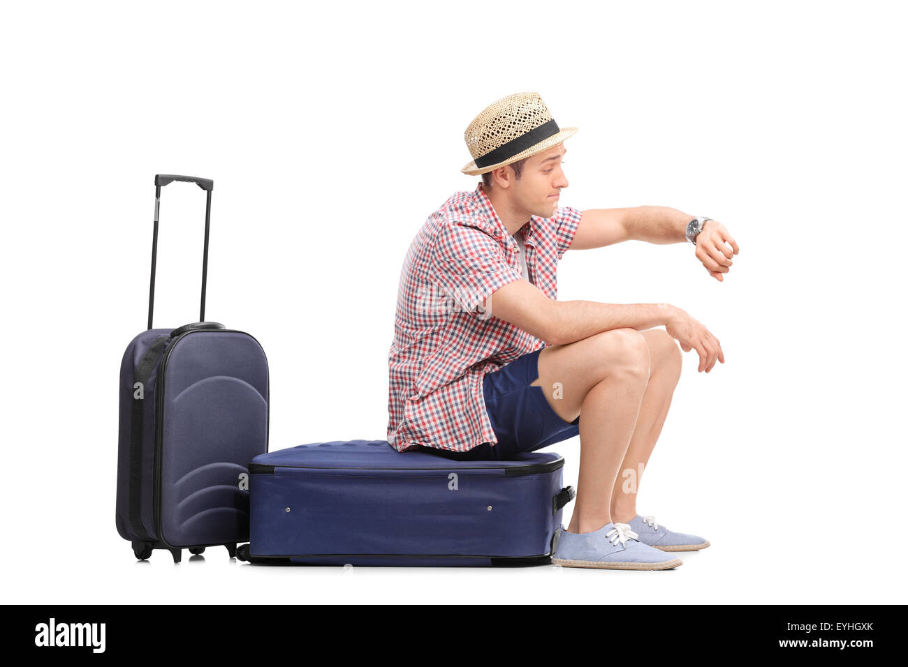 Junge männliche Touristen sitzen auf seinem Gepäck und mit Blick auf die Zeit, die isoliert auf weißem Hintergrund Stockfoto
