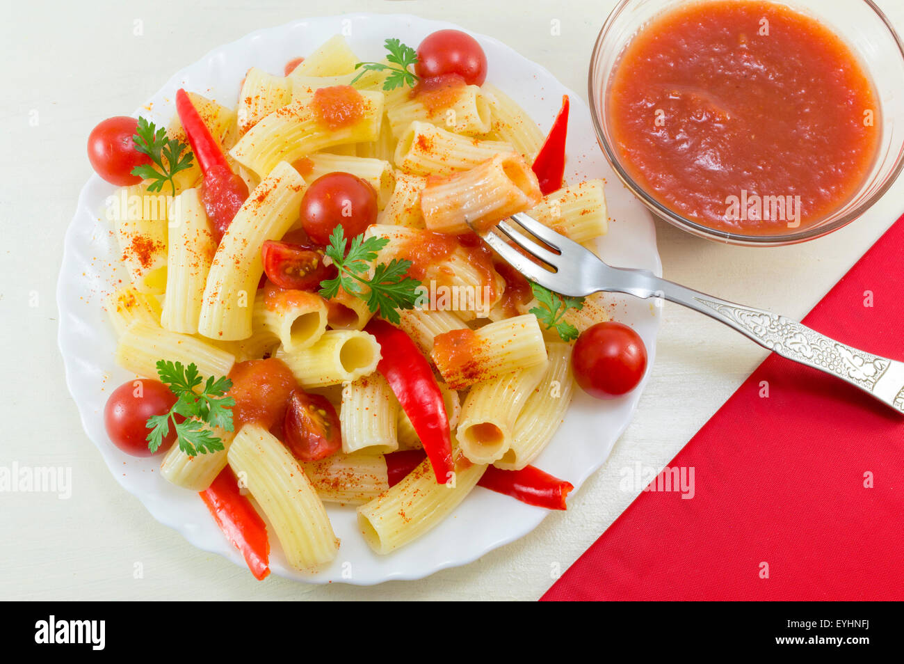 Makkaroni mit Cherry-Tomaten, Petersilie und Paprika serviert mit Tomatensauce und einer Gabel auf einem Tisch mit roten Serviette Stockfoto