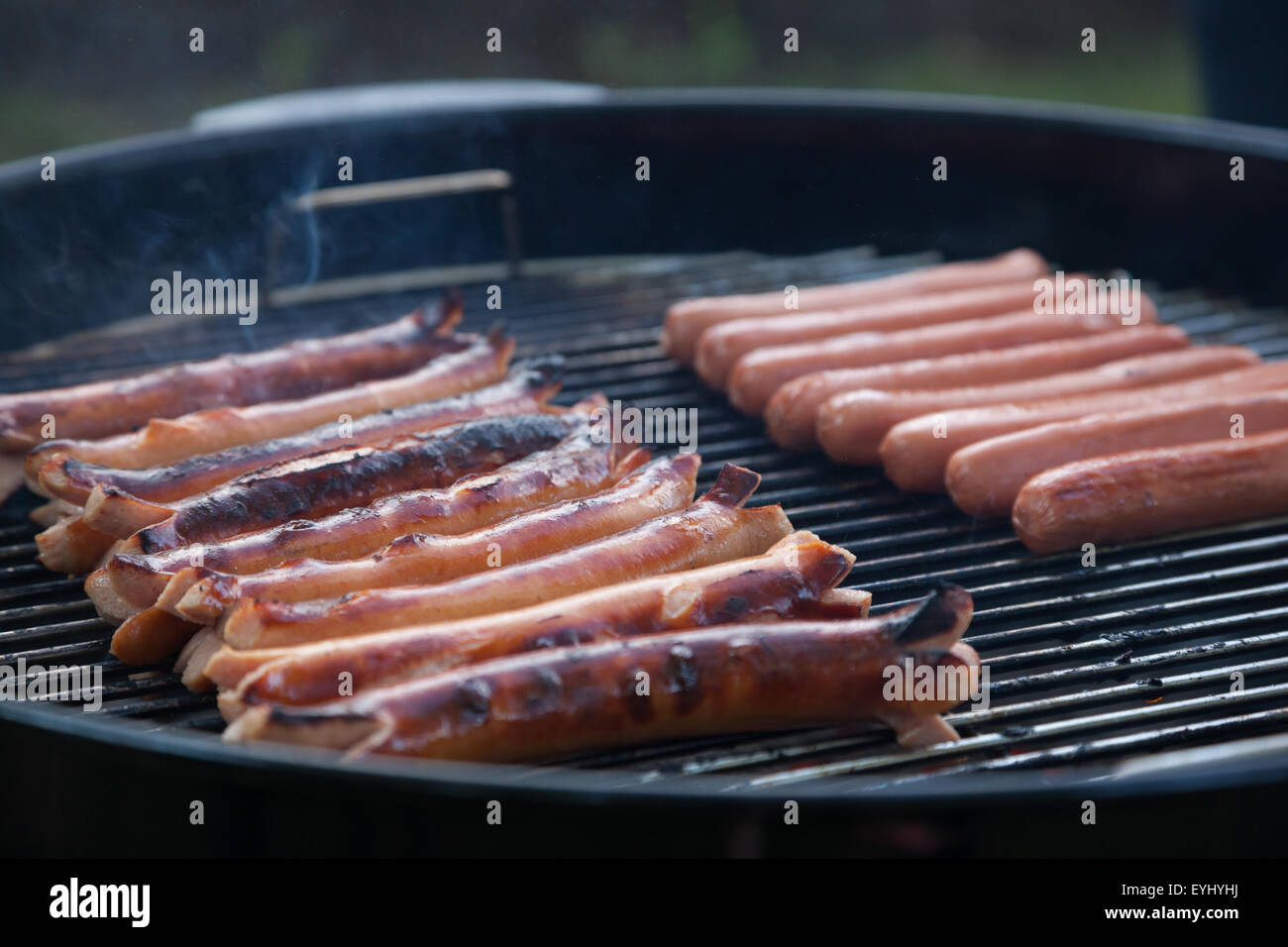 Mehrere heiße Hunde sitzen auf einem Rauchen Holzkohle Grill Kochen Stockfoto