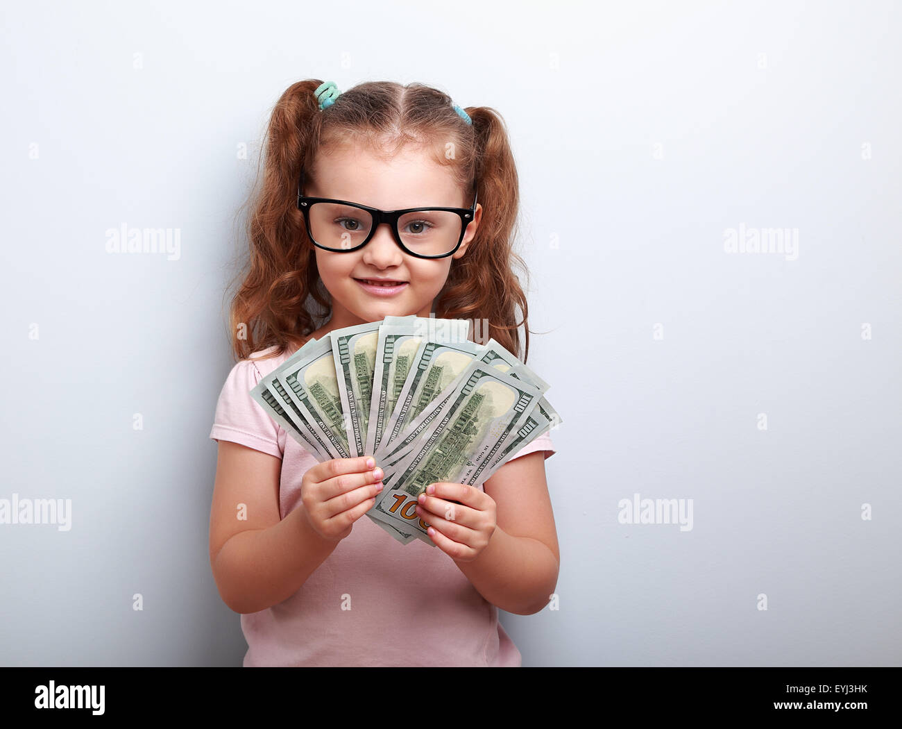 Glückliches Kind Mädchen in Gläsern, die Geld in die Hand und suchen mit Lächeln auf blauem Hintergrund mit leeren Textfreiraum Stockfoto