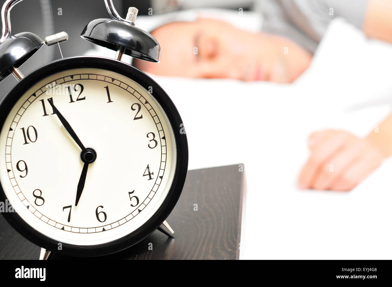 Nahaufnahme eines Weckers auf 6,55 morgens auf dem Nachttisch und ein junger kaukasischen Mann schlafend im Bett Stockfoto