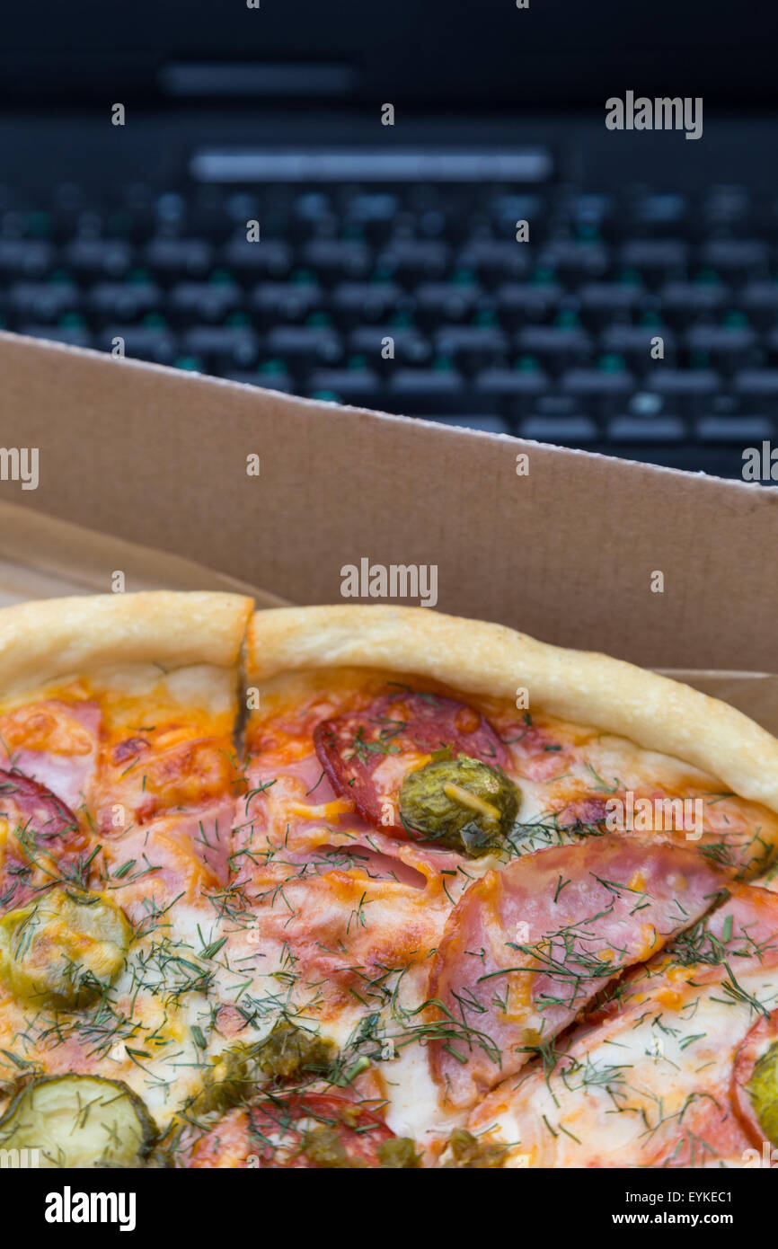 Stück Pizza mit Wurst und Speck in Box auf Laptop Tastatur Hintergrund Stockfoto