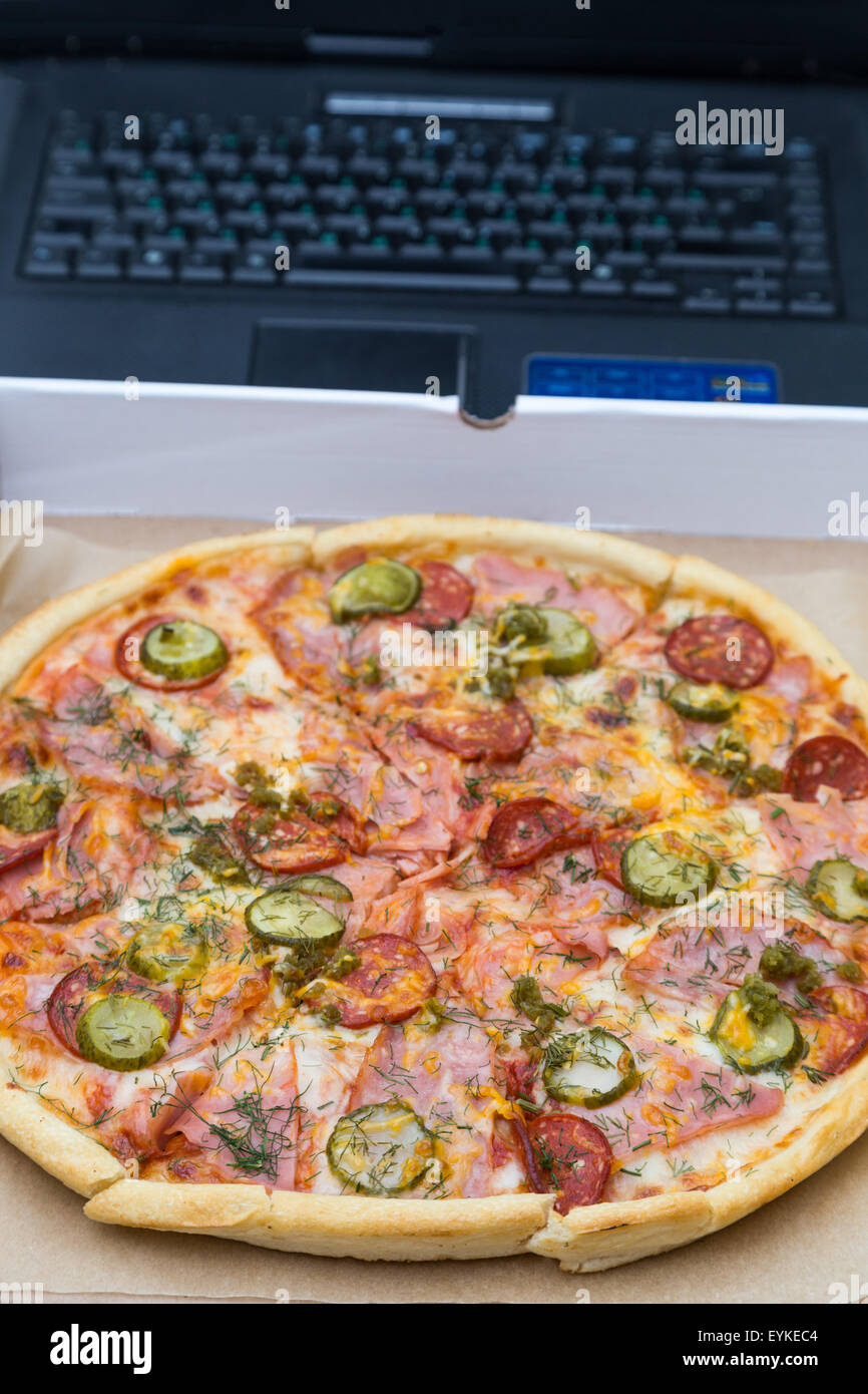 Stück Pizza mit Wurst und Speck in Box auf Laptop Tastatur Hintergrund Stockfoto
