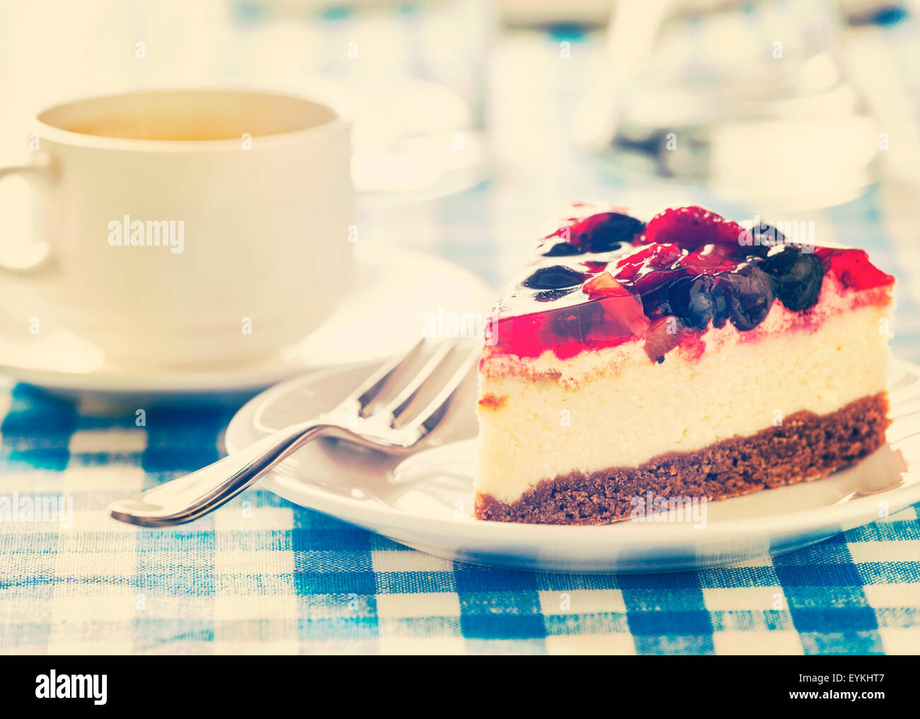 Vintage retro-Effekt gefilterte Hipster Stil Bild Dessert Obst Käse Kuchen auf Teller mit Gabel und Kaffee Tasse auf blau-checker Stockfoto