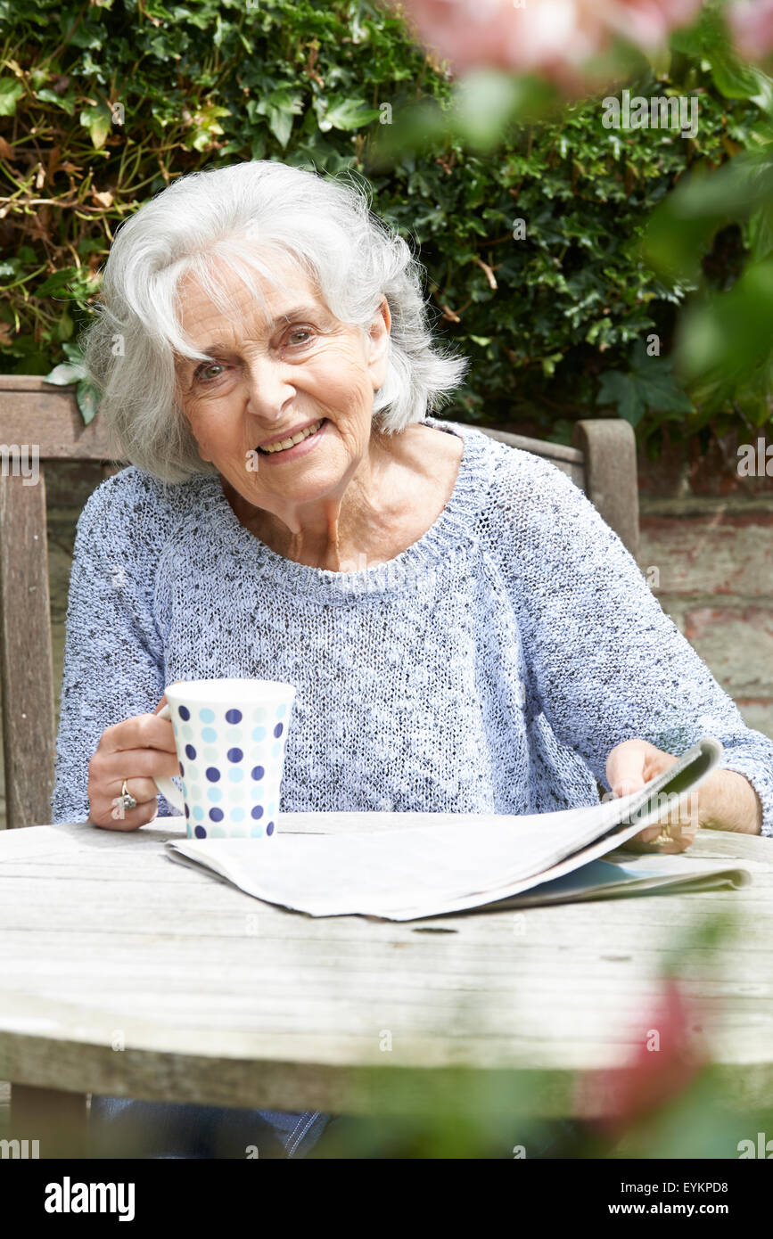 Portrait Of Senior Woman entspannend im Garten lesen Zeitung Stockfoto