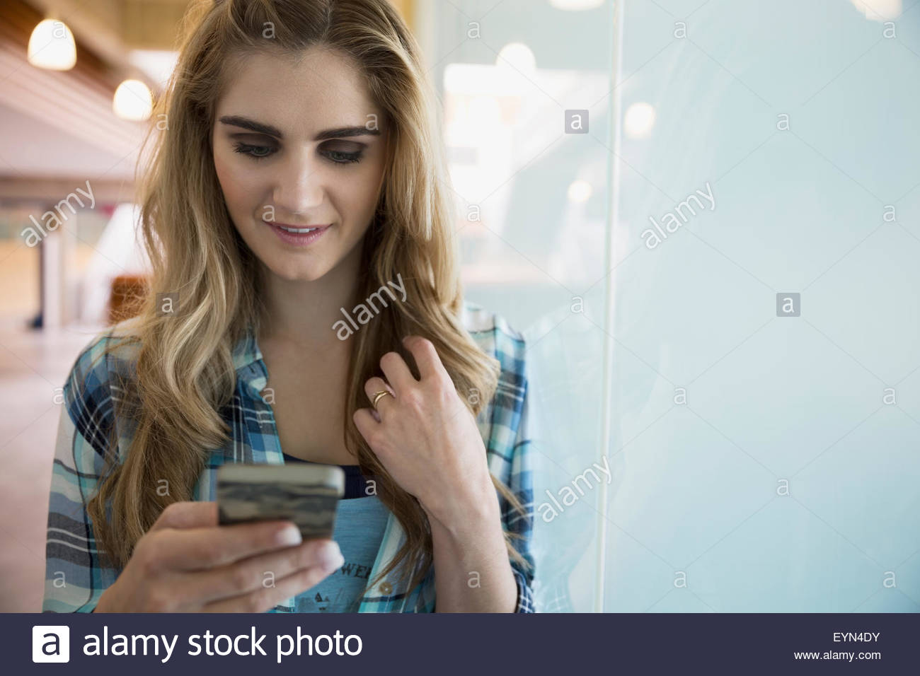 Blonde Frau SMS mit Handy am Fenster Stockfoto