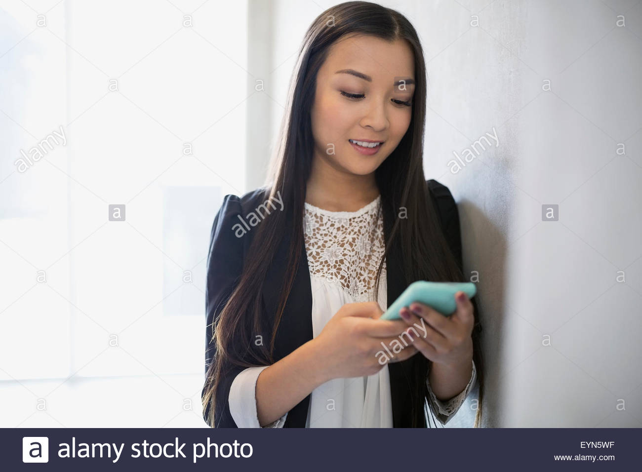 Frau SMS mit Handy an die Wand gelehnt Stockfoto