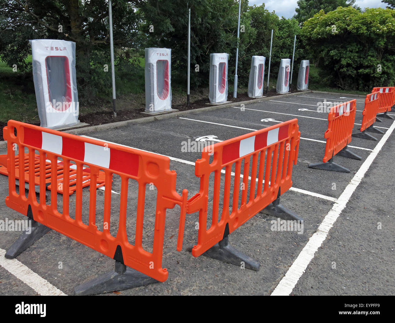 Tesla Ladestationen auf einer Autobahnraststätte in Großbritannien, mit Barrieren um umgesetzt werden Stockfoto