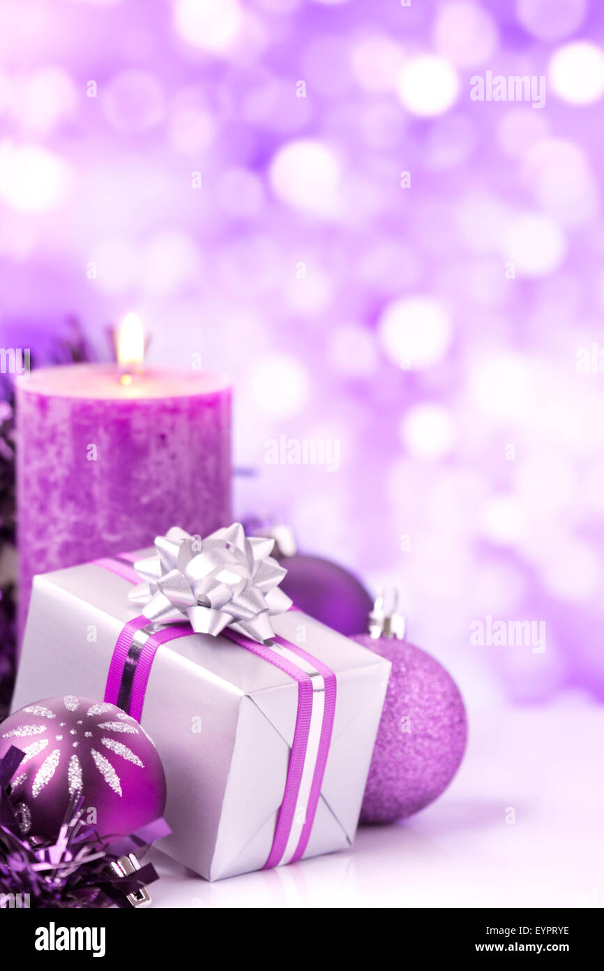 Lila und Silber Weihnachtskugeln, ein Geschenk und eine Kerze vor defokussierten lila und weißen Lichter. Stockfoto