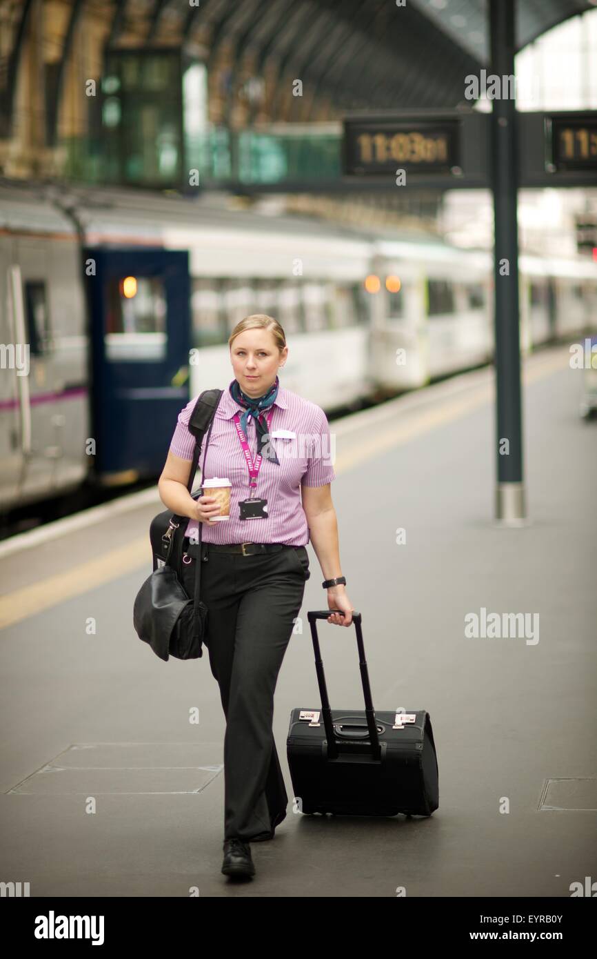 Weibliche Eisenbahnarbeiter geht eine Plattform bereit, einen Zug mit Koffer und Kaffee in der Hand am Bahnhof King's Cross in London, Großbritannien Stockfoto