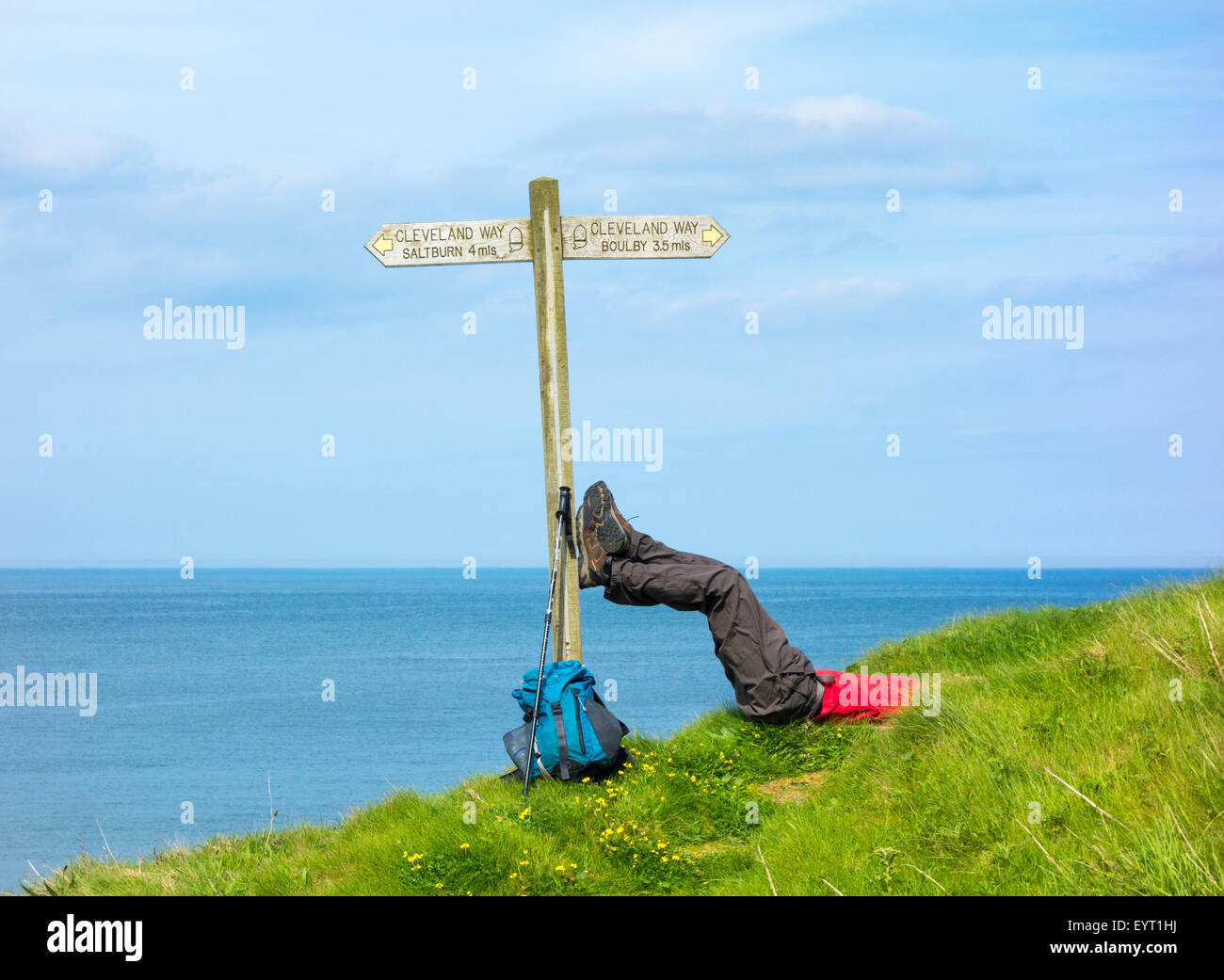Männliche Wanderer ruht mit Füßen auf Wegweiser am Skinningrove zwischen Saltburn und Staithes auf The Cleveland Way Trail. UK Stockfoto