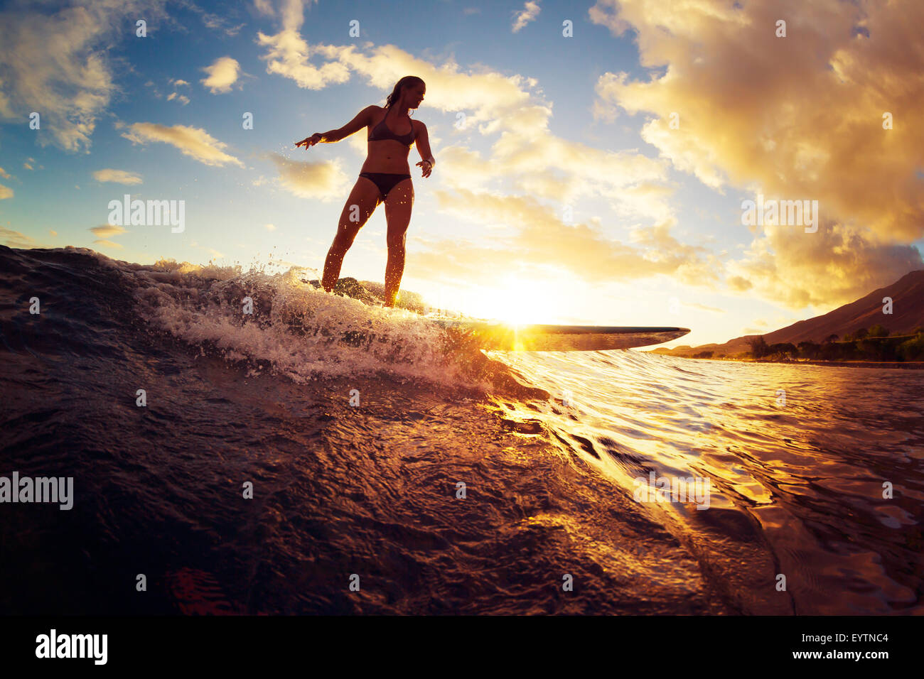 Surfen bei Sonnenuntergang. Schöne junge Frau Welle bei Sonnenuntergang zu reiten. Outdoor-aktiven Lebensstil. Stockfoto