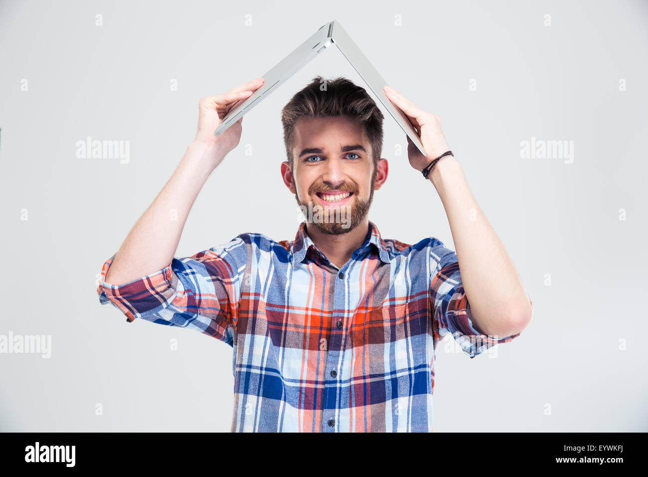 Glücklicher Mann mit Laptop auf dem Kopf wie Dach des Hauses isoliert auf einem weißen Hintergrund. Blick in die Kamera Stockfoto