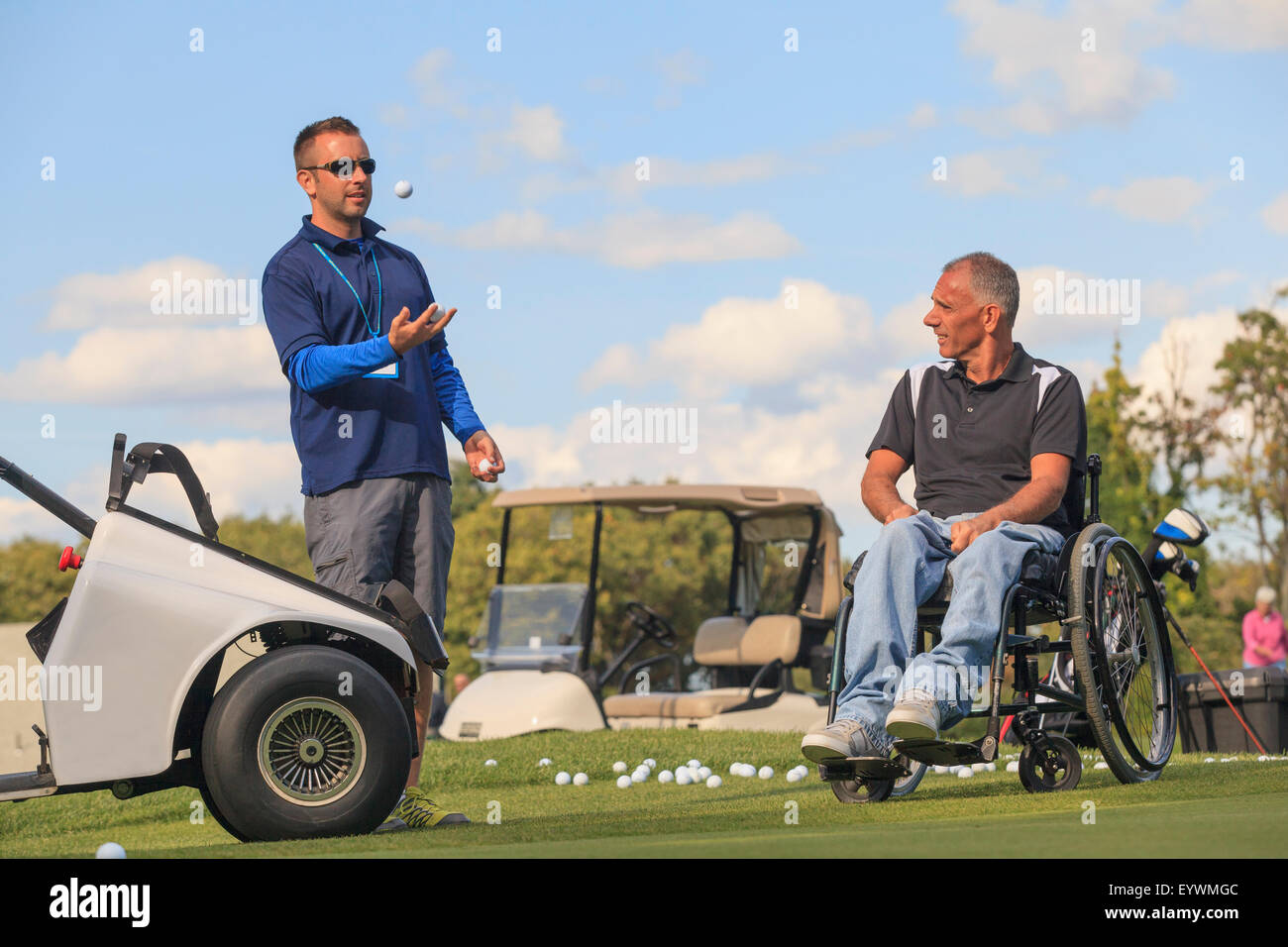 Mann mit einer Rückenmarksverletzung in eine adaptive Warenkorb zusammen mit seinem Assistenten Golf spielen Stockfoto