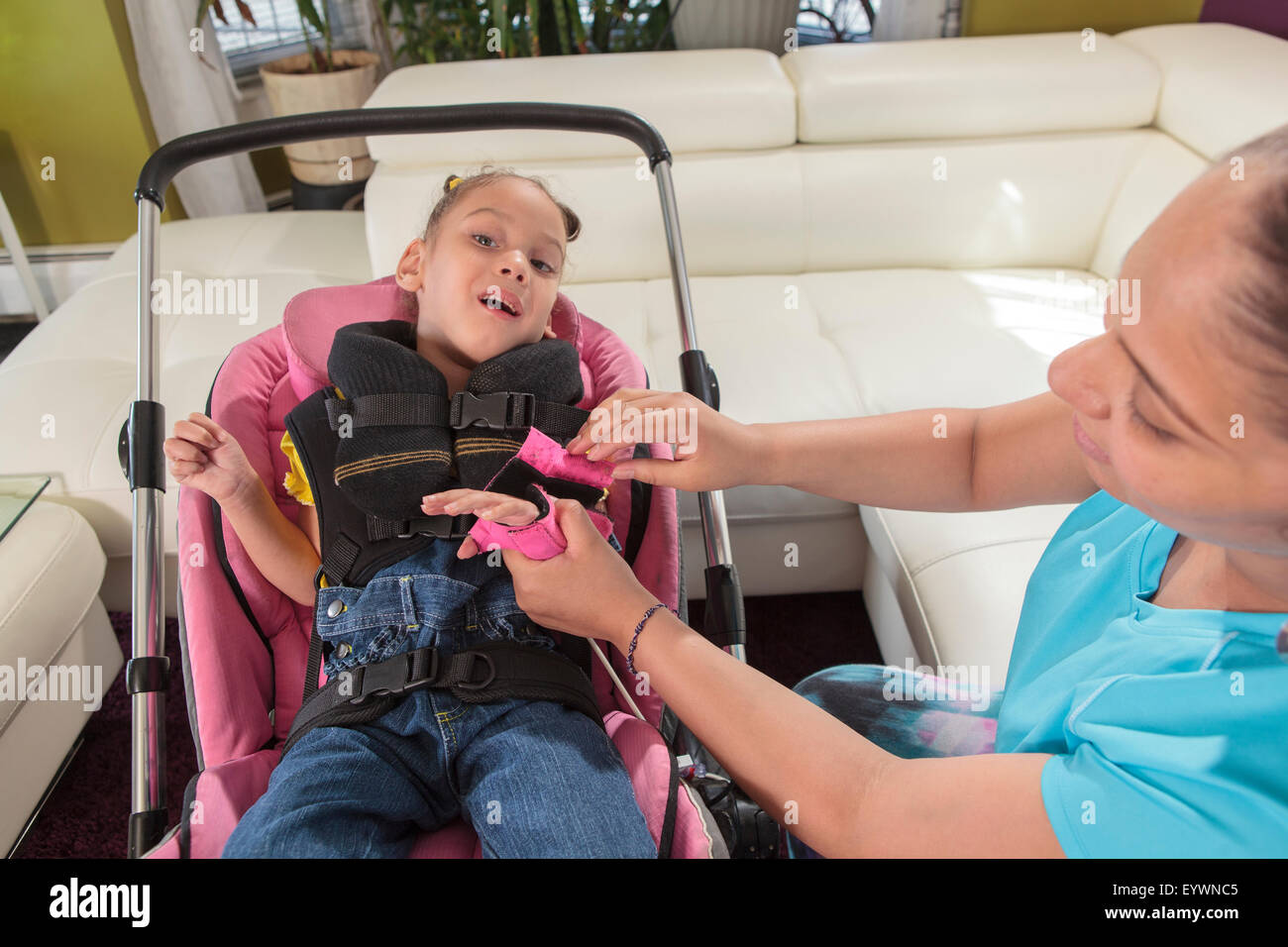 Mutter, die kleine Tochter mit Zerebralparese in Kinderwagen gehen Hand Bandage anziehen Stockfoto