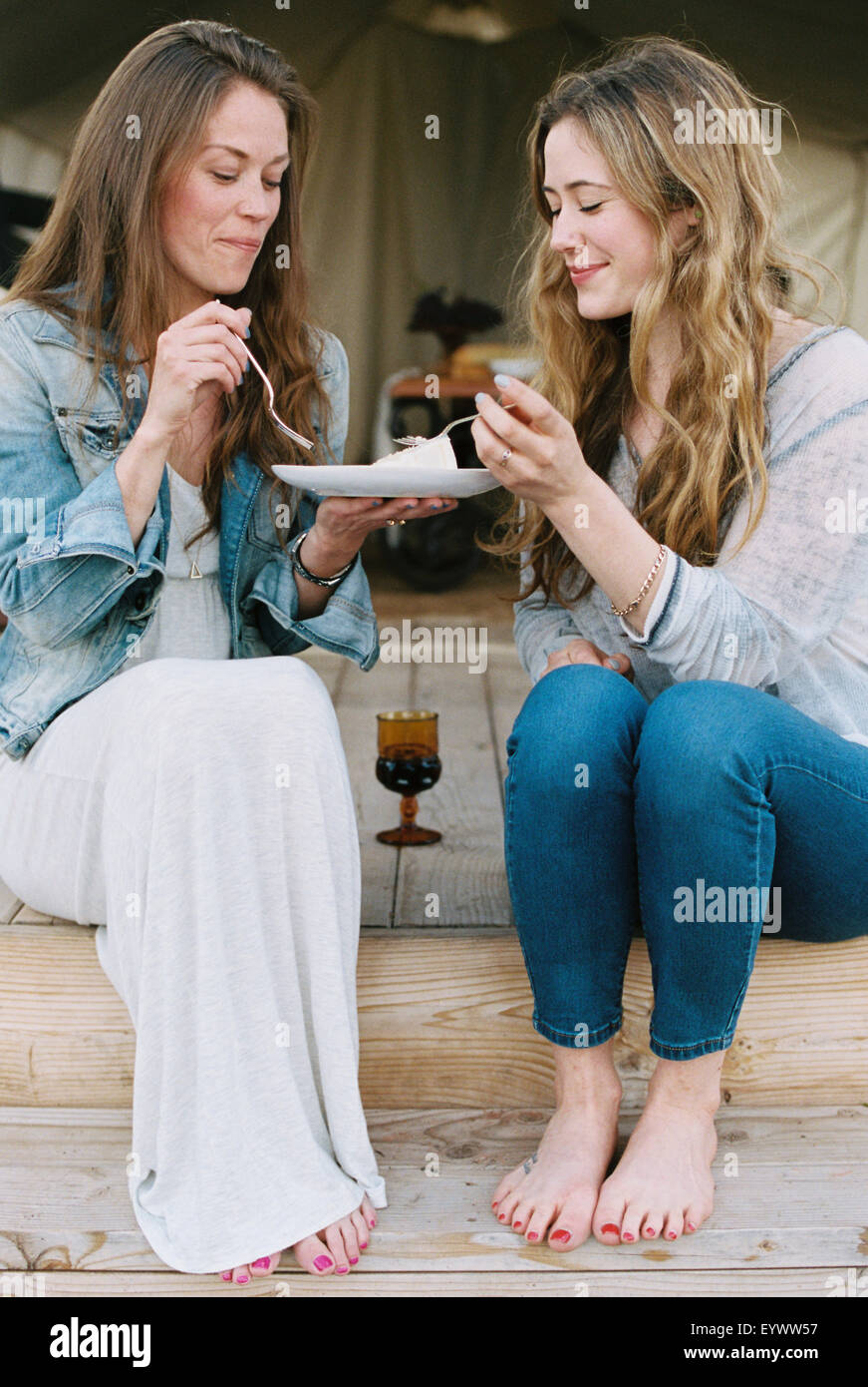 Zwei Frauen sitzen im Freien, Austausch von Kuchen und einem Glas Wein. Stockfoto