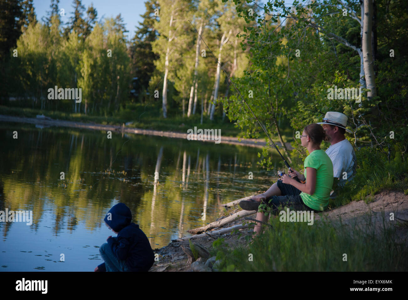 Ein Mädchen und ihr Vater in einem schönen reflektierende Bergsee Fischen.  Das glatte Wasser reflektiert die Bäume in der Abendsonne Stockfoto