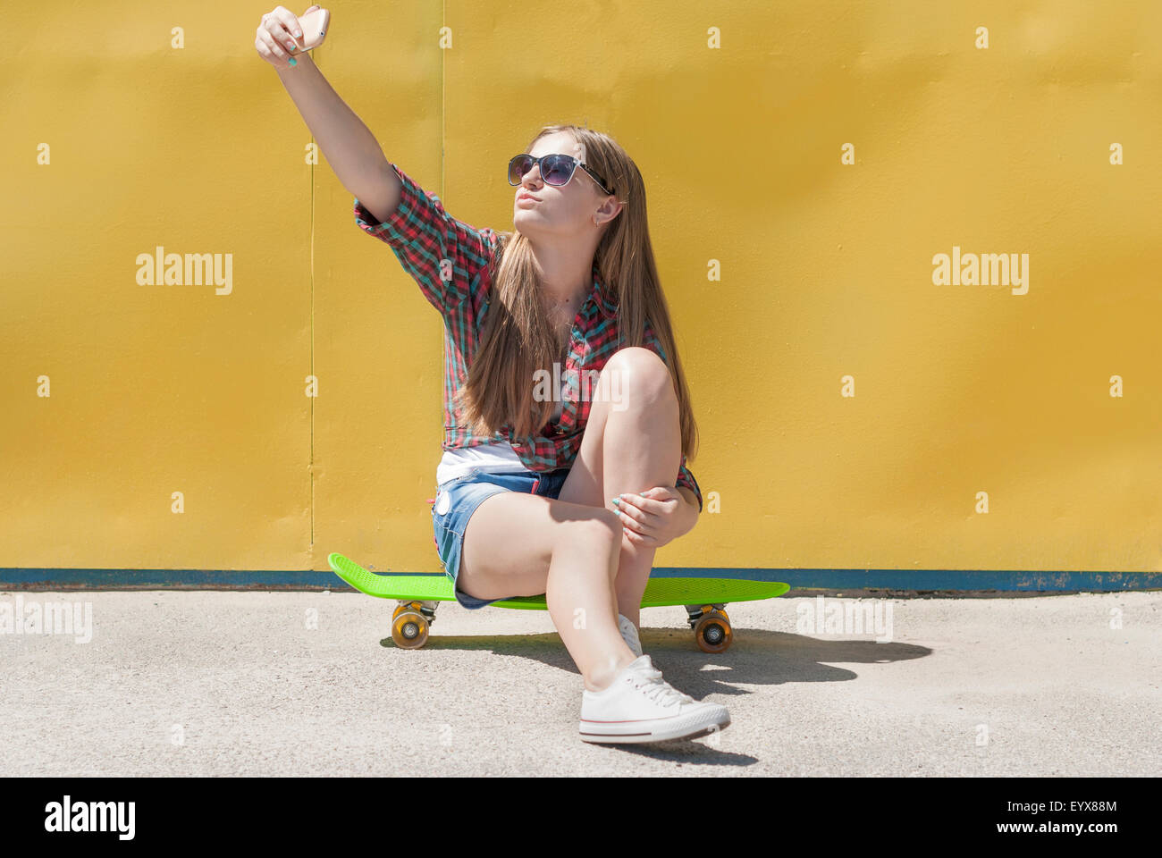 Stilvolles junge Mädchen sitzt auf einem Skateboard macht ein Selbstporträt-Handy. Stockfoto