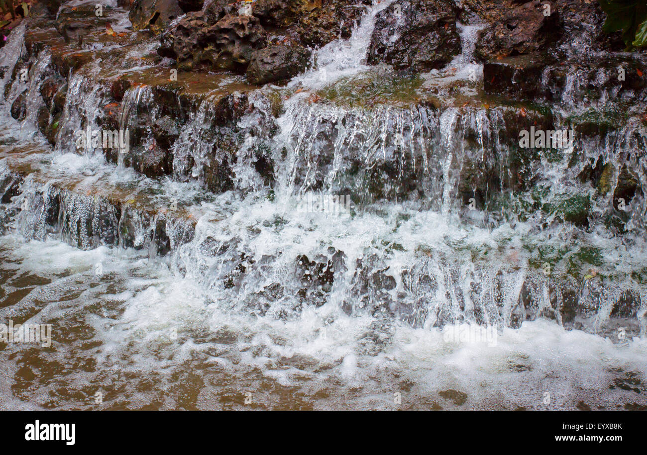 Wasser sanft Kaskadierung über Schichten von Gestein in einem seichten Teich Stockfoto