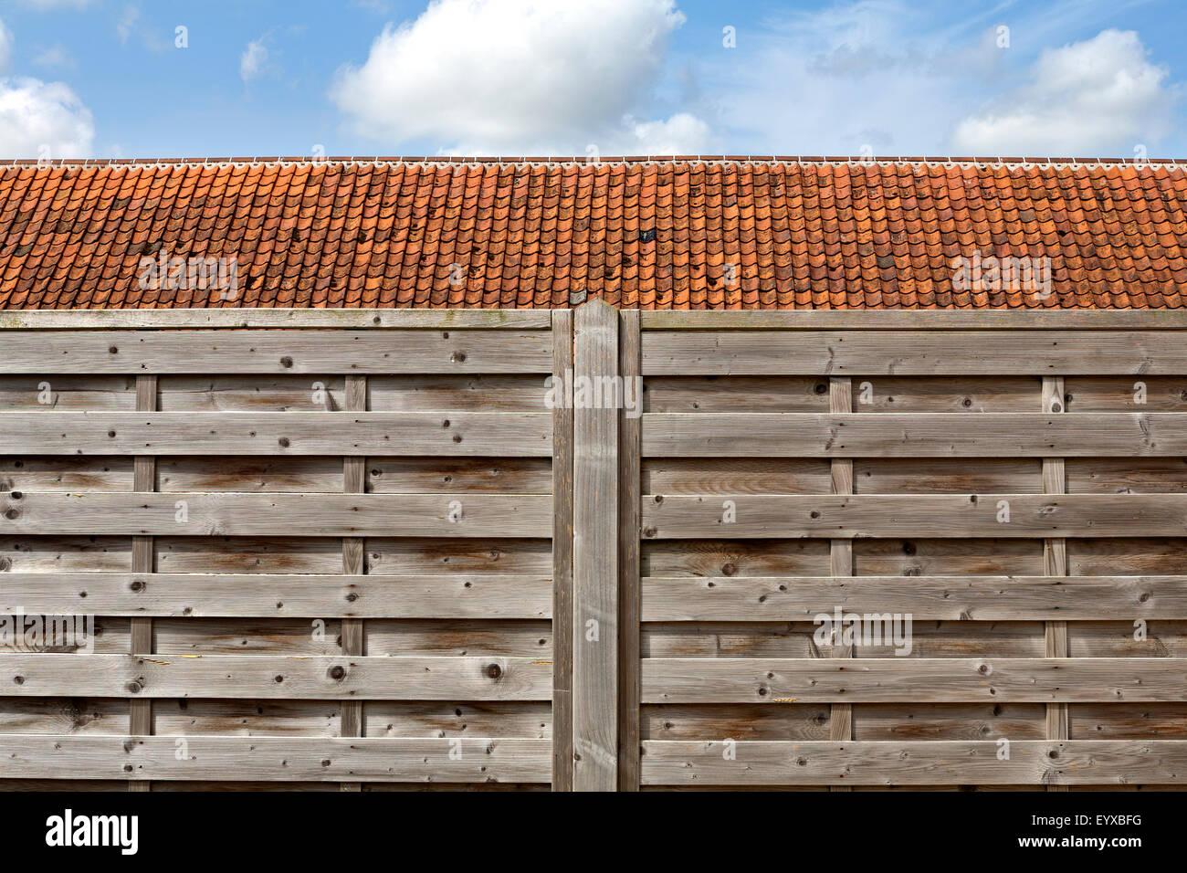 Geradeaus weiter Schuss von Lattenrost aus Holz Zaun vor einem pantiled Dach vor einem blauen leicht bewölktem Himmel Norfolk England Stockfoto