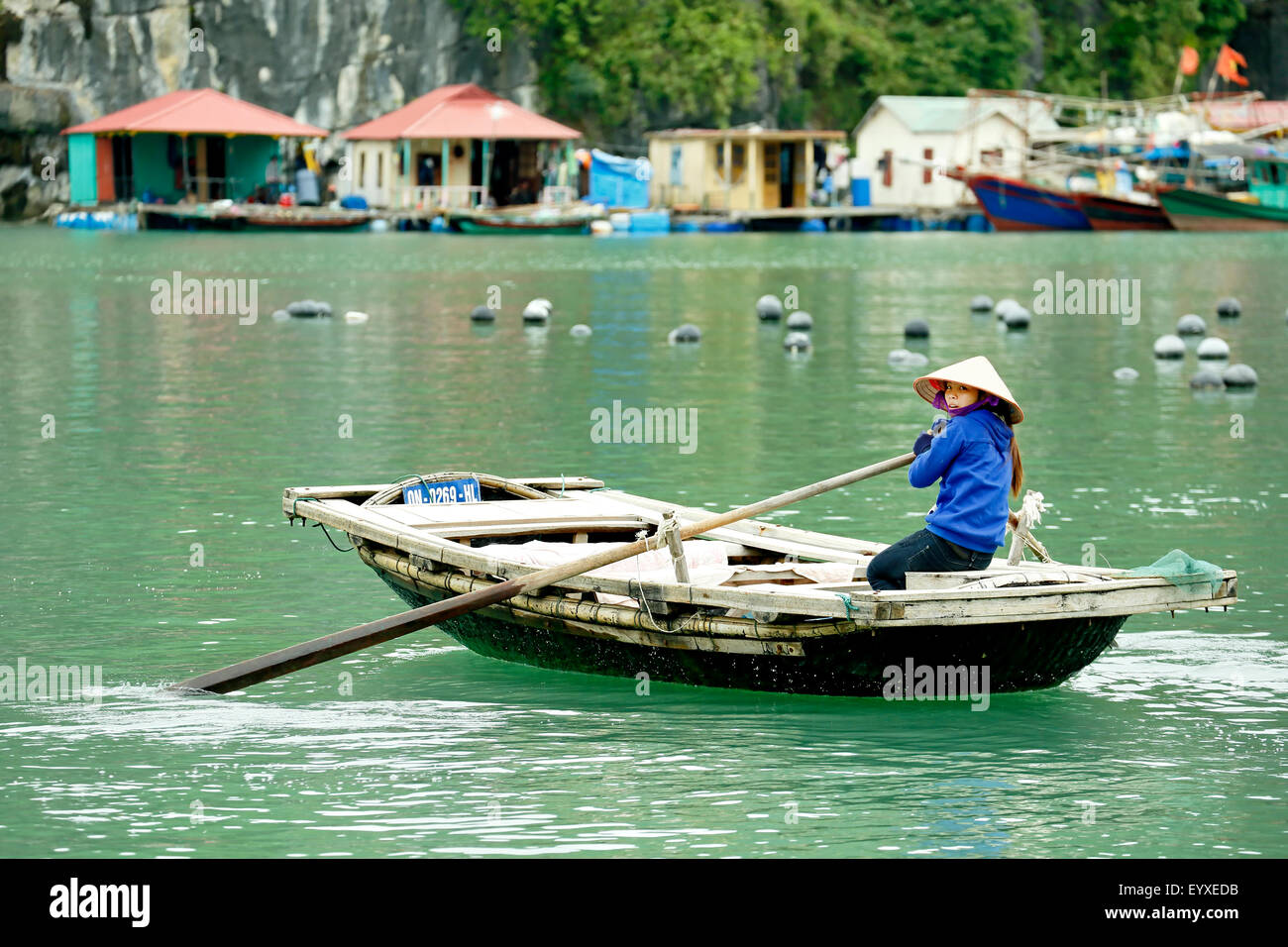 Frau aus Holz Ruderboot Rudern und schwimmende Häuser, Vung Vieng Fischerdorf, Ha Long Bucht, Bai Tu Long Sektor, Vietnam Stockfoto
