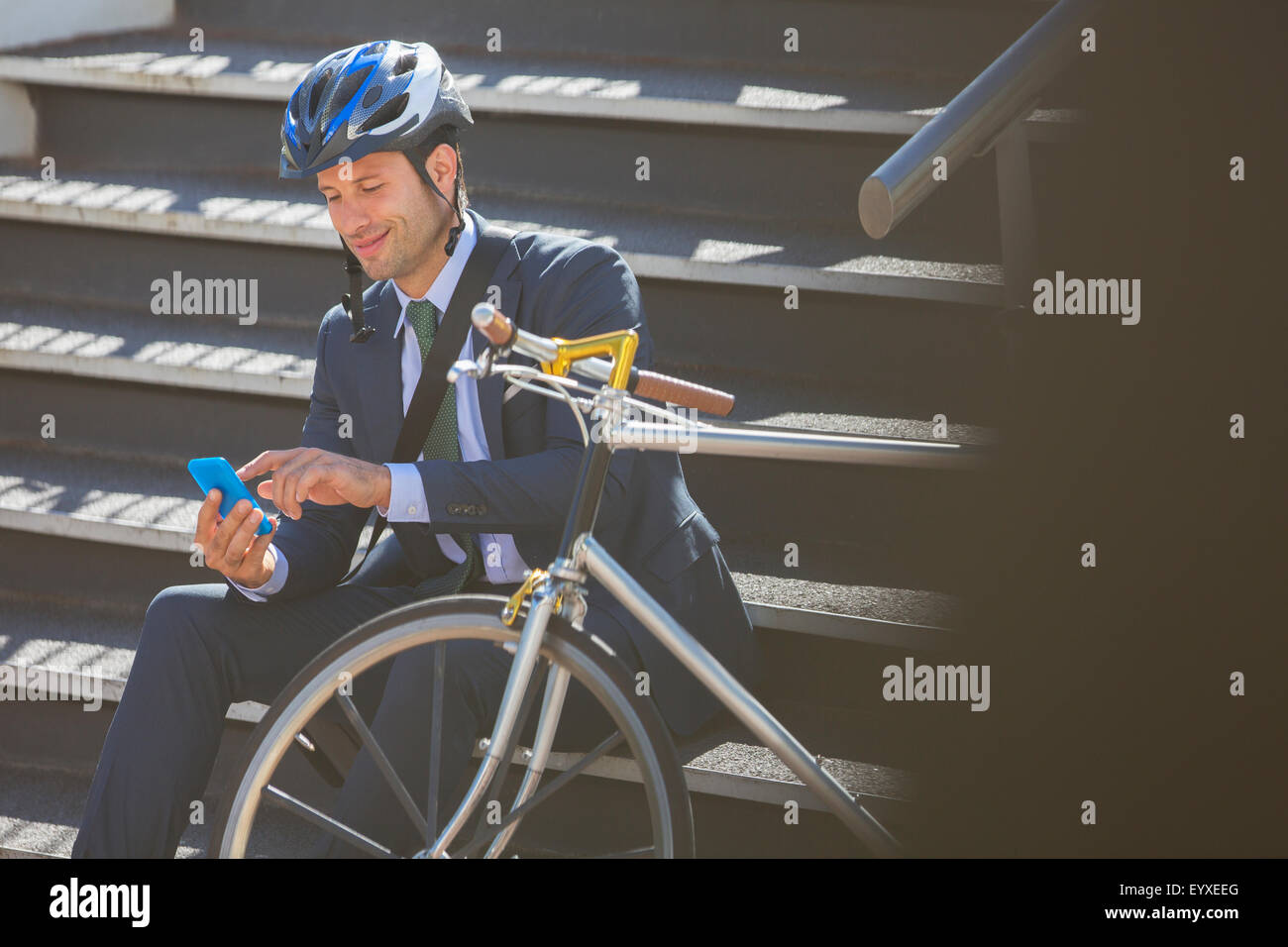 Geschäftsmann im Anzug mit Fahrrad und Helm SMS mit Handy auf Treppe Stockfoto