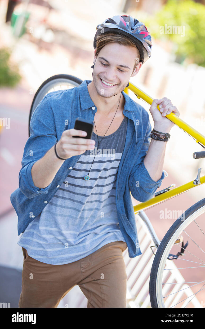 Junger Mann mit Helm mit Fahrrad und SMS auf Handy Stockfoto