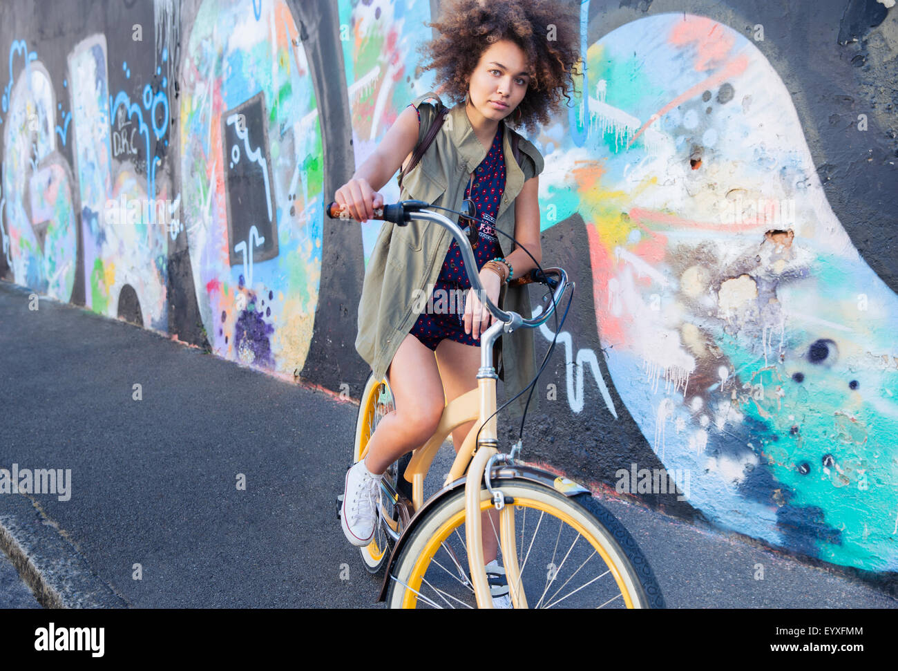 Porträt Ernst Frau mit Afro auf dem Fahrrad neben urban Graffitiwand Stockfoto