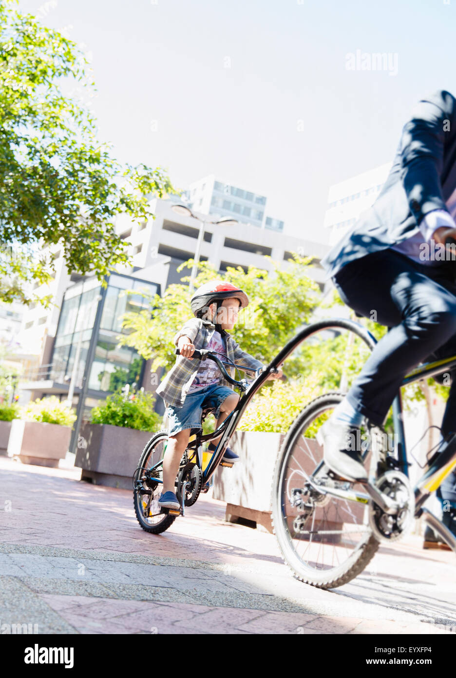 Sohn im Helm Tandem Fahrrad mit Geschäftsmann Vater im sonnigen Stadtpark Stockfoto