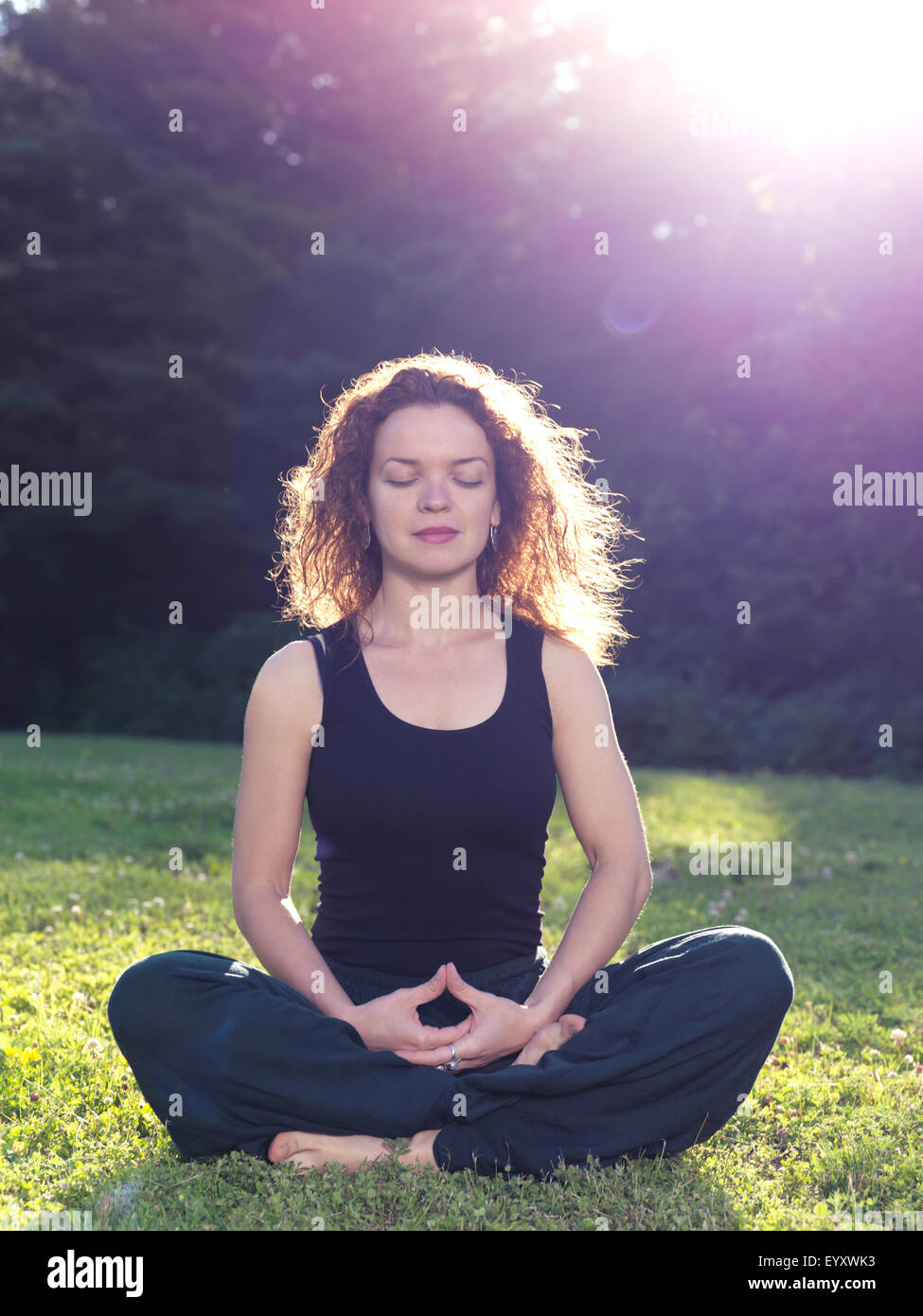 Führerschein erhältlich unter MaximImages.com - Frau meditiert in der Natur, sitzt auf Gras im Sonnenlicht Stockfoto