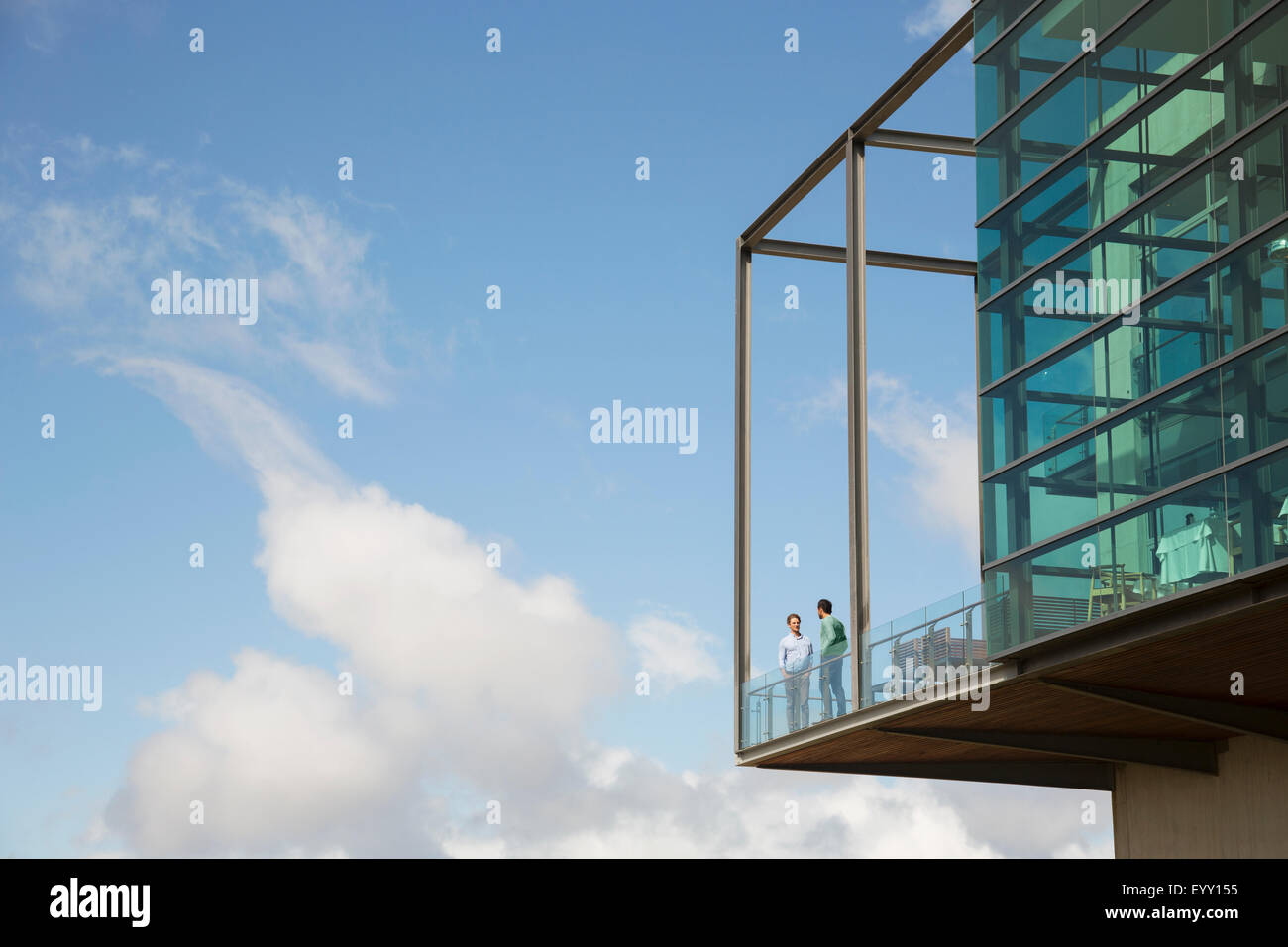 Männer sprechen auf Balkon Glas stoßen gegen blauen Himmel Stockfoto