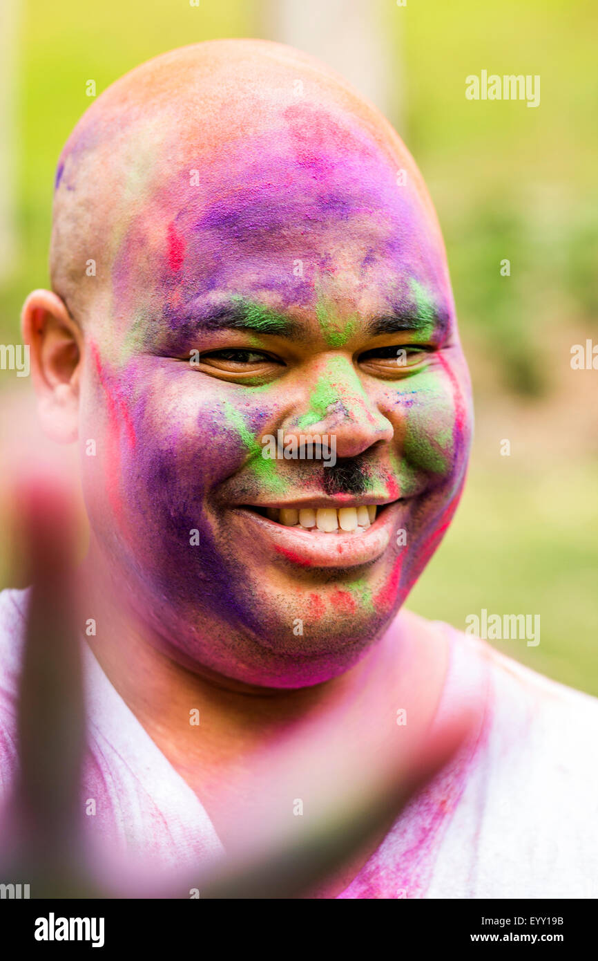 Lächelnder Mann bedeckt in Pigment Pulver gestikulieren Friedenszeichen, Stockfoto