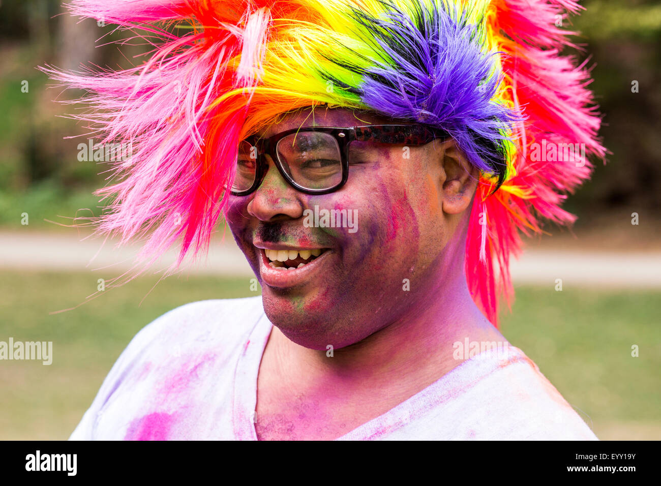 Lächelnder Mann bedeckt in Pigmentpulver tragen mehrfarbige Perücke Stockfoto