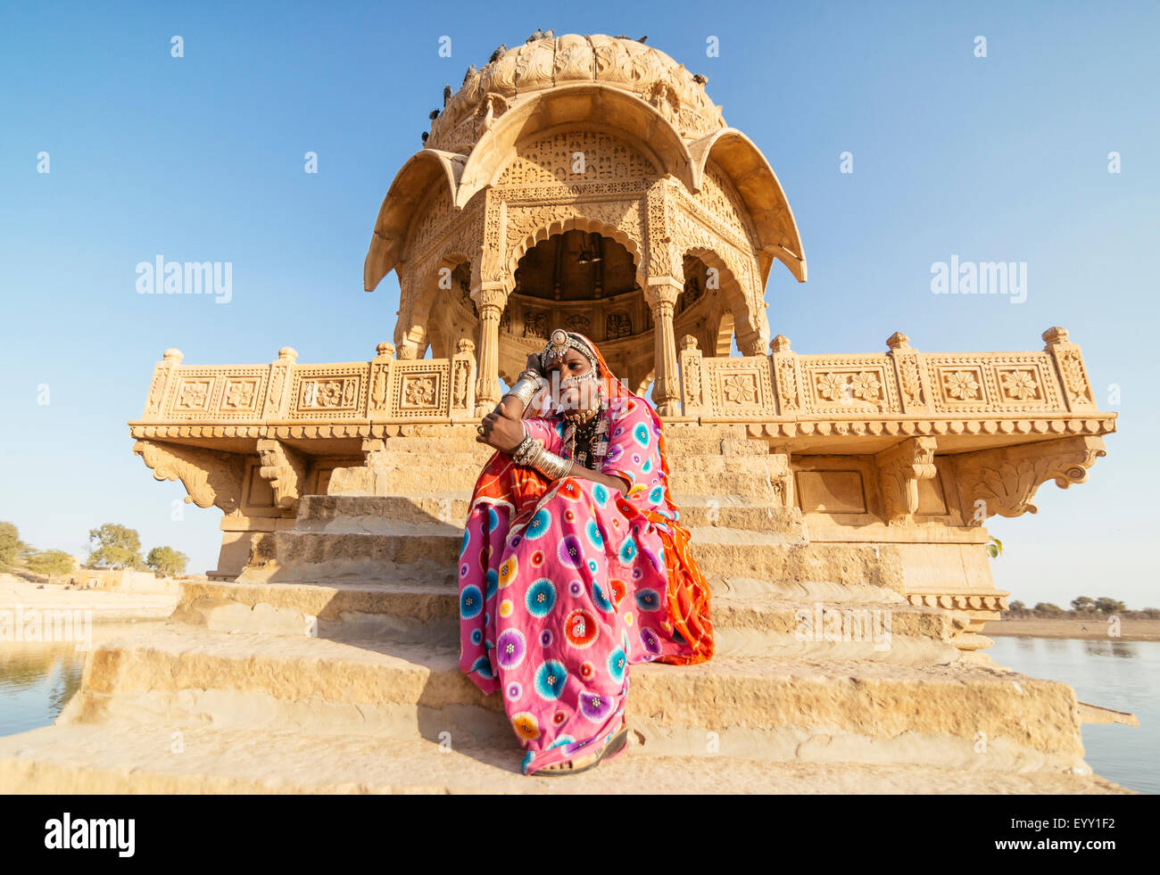 Indische Frau in traditioneller Kleidung, die sitzt in der Nähe von Denkmal, Jaisalmer, Rajasthan, Indien Stockfoto