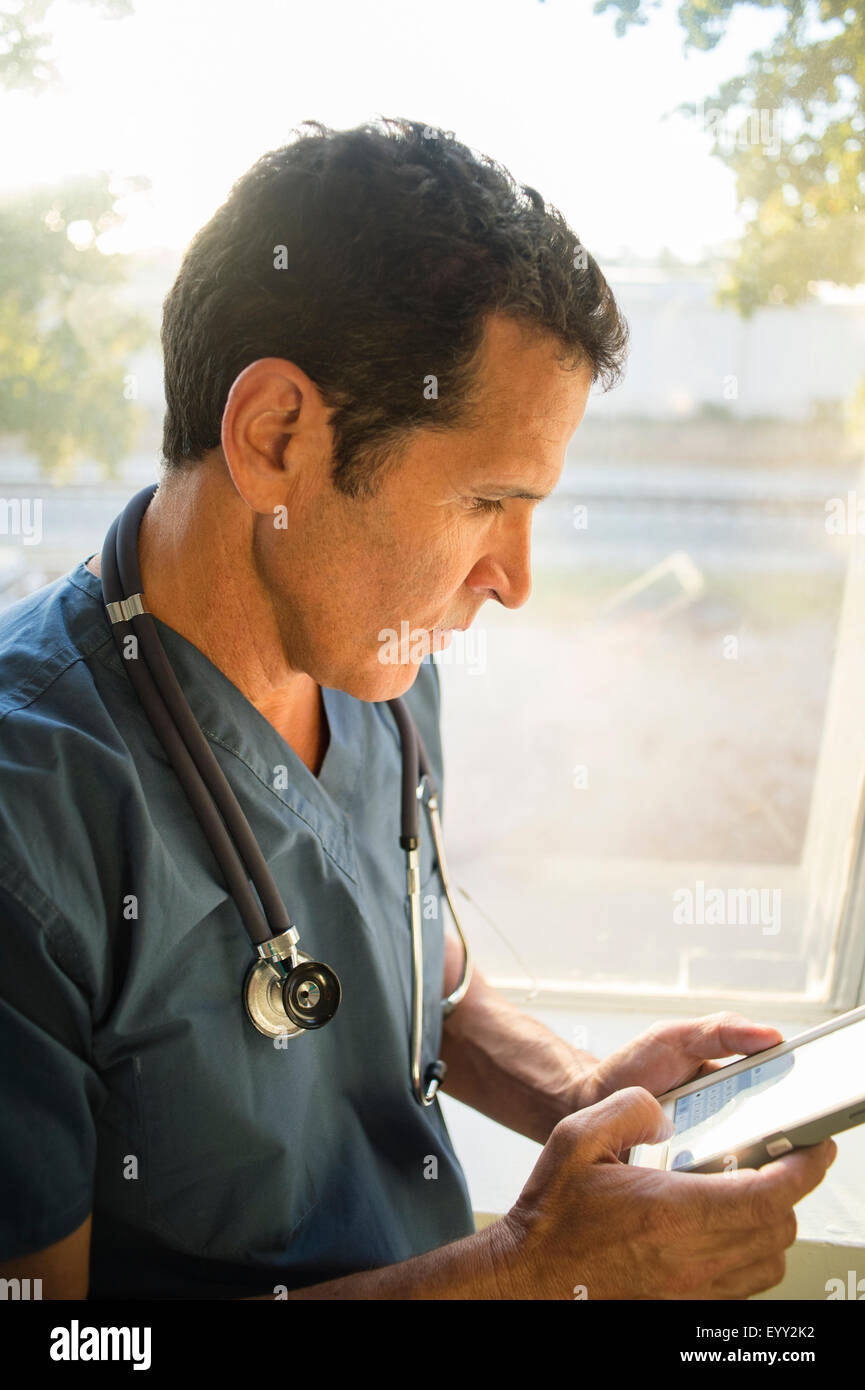 Hispanische Arzt mit Handy in der Nähe von Fenster Stockfoto