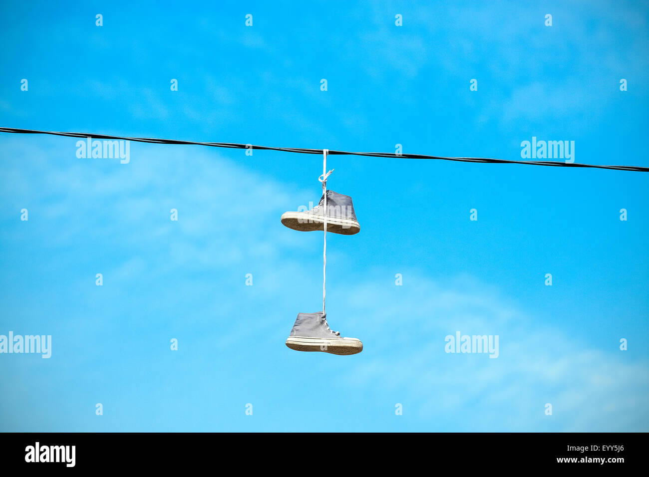 Alte Schuhe hängen an einem elektrischen Kabel gegen blauen Himmel. Stockfoto