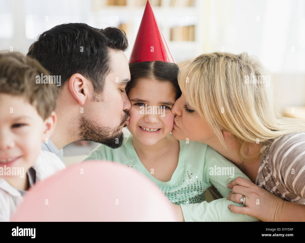 Kaukasische Eltern küssen Tochter auf Geburtstagsparty Stockfoto