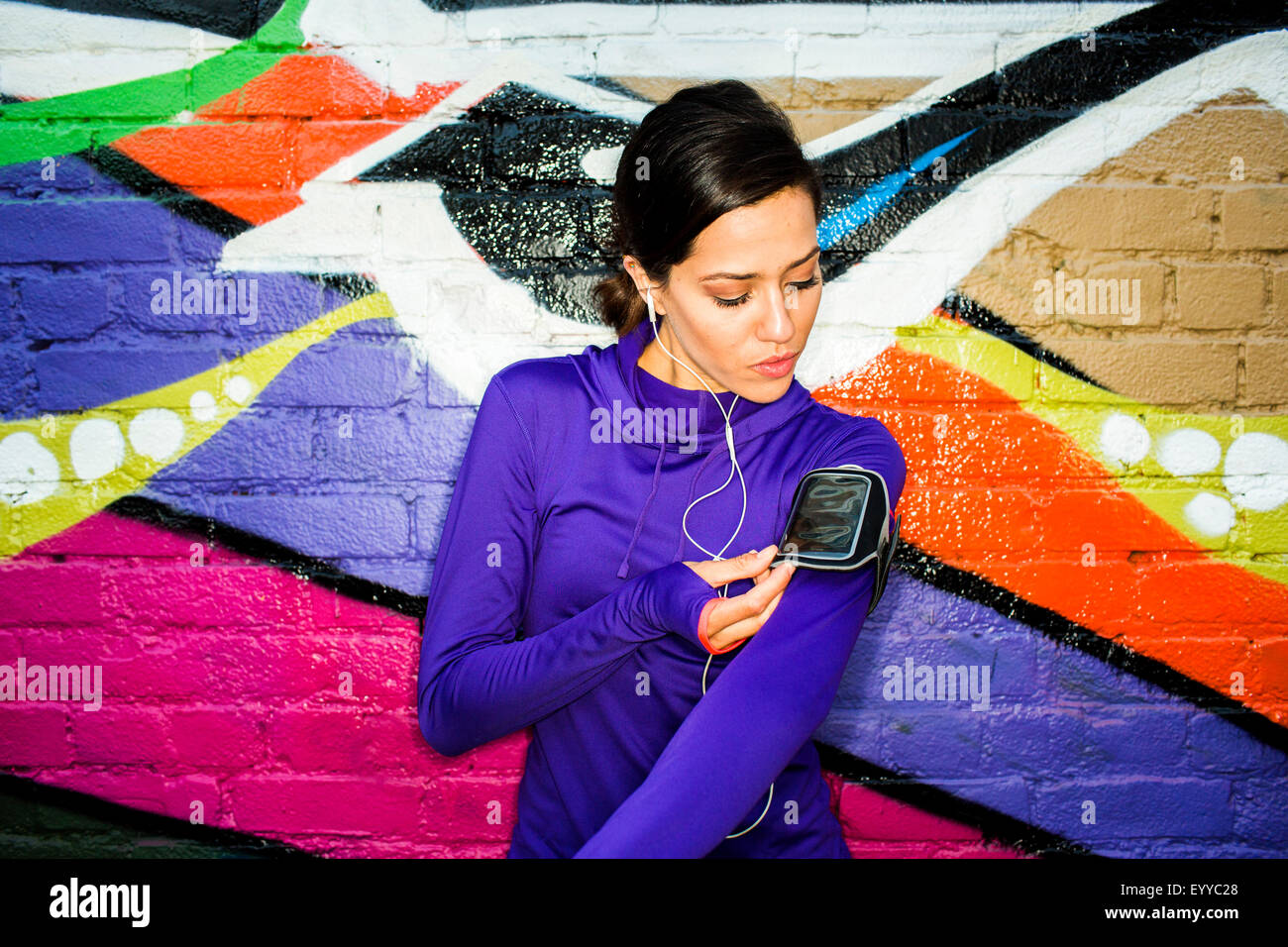 Hispanische Läufer mit Handy in der Nähe von Graffitiwand Stockfoto