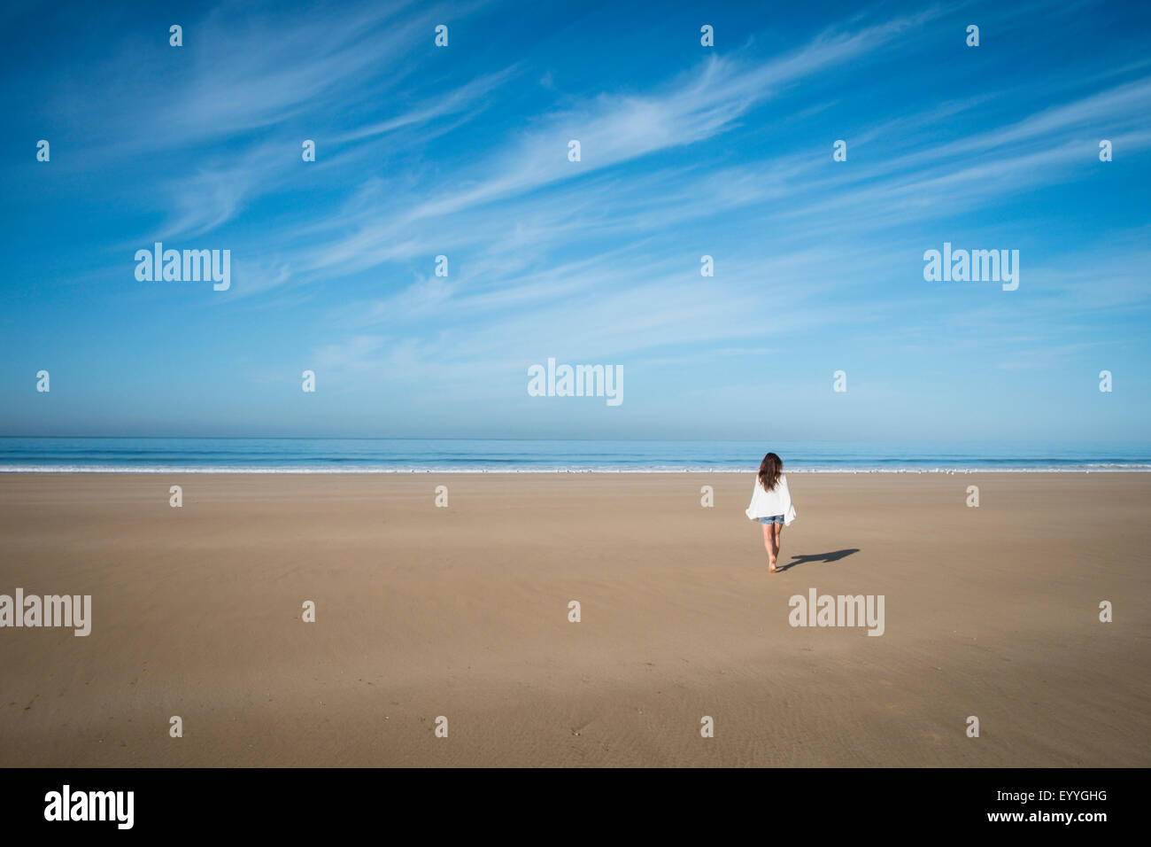 Kaukasische Frau zu Fuß am Strand unter blauem Himmel Stockfoto
